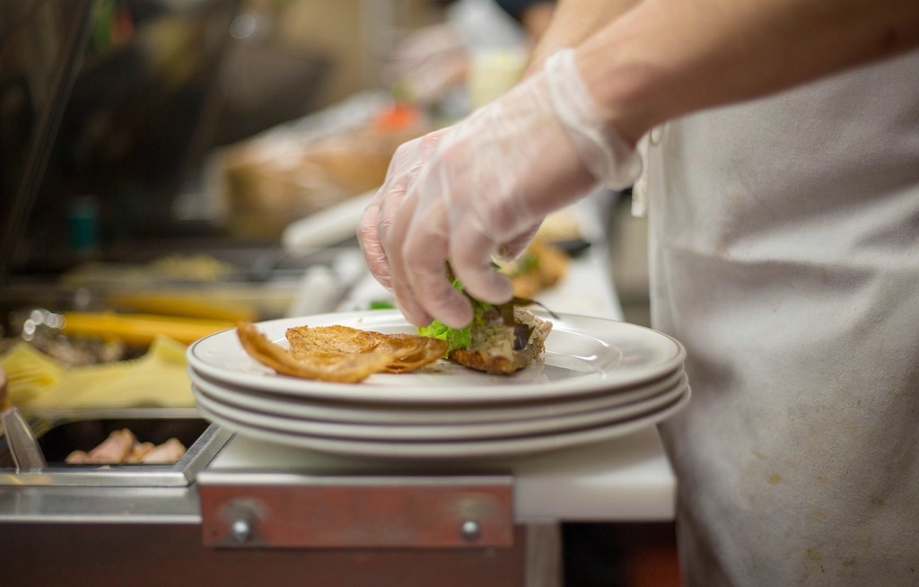 A cook in gloves finishing a plate at a restaurant kitchen counter
