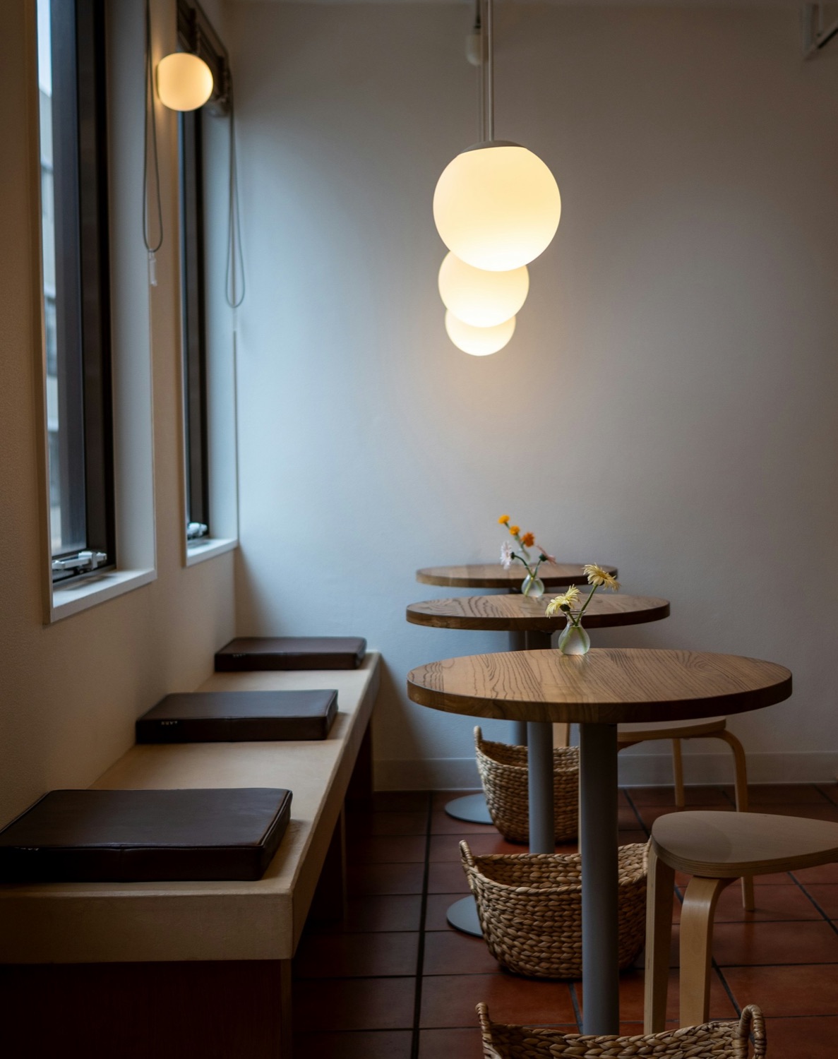 A small, warmly lit café with round wooden tables and a window bench
