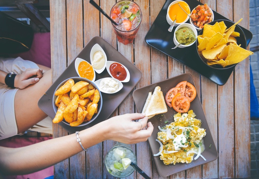 Plates of potato wedges, dips, nachos and eggs shared across a wooden table